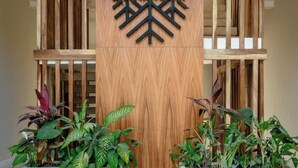 Un espace d’accueil agrémenté d’un panneau en bois sur lequel figure le nom « CASAVANGAR » et d’un logo moderne aux formes géométriques. De part et d’autre, on trouve deux grands bacs à plantes contenant des végétaux verts.