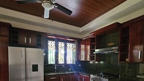 A kitchen with wooden cabinets, a stainless steel refrigerator, a gas stove, and a ceiling fan. - Apartamento Fresco y Seguro con Piscina y Terrazas, 1 Hora las Mejores Playas (Managua)
