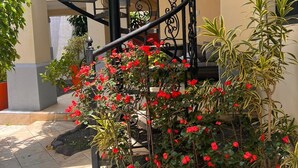 A spiral staircase with a wrought iron railing, surrounded by a garden with red flowers and various plants. - Apartamento Fresco y Seguro con Piscina y Terrazas, 1 Hora las Mejores Playas (Managua)