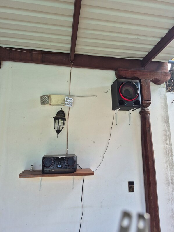 A room with a ceiling fan, a wall-mounted speaker, a shelf with electronic devices, and a wall-mounted light fixture.