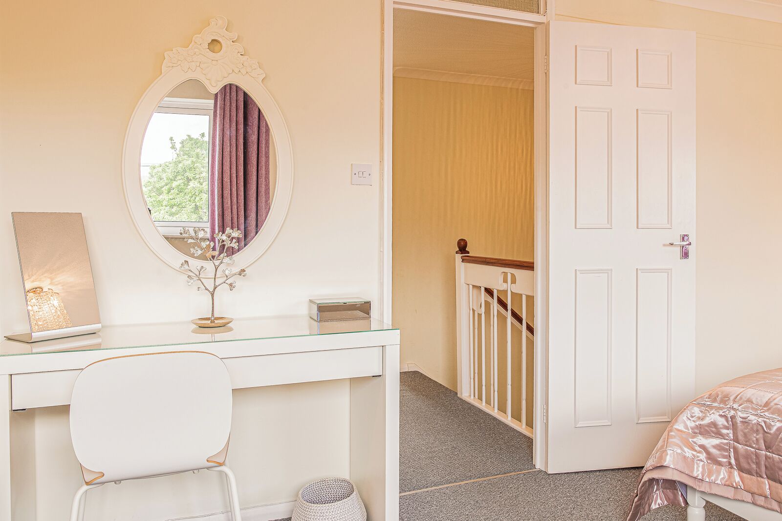 A bedroom with a white bed, a bedside table with a lamp, a mirror, and a door leading to a staircase.