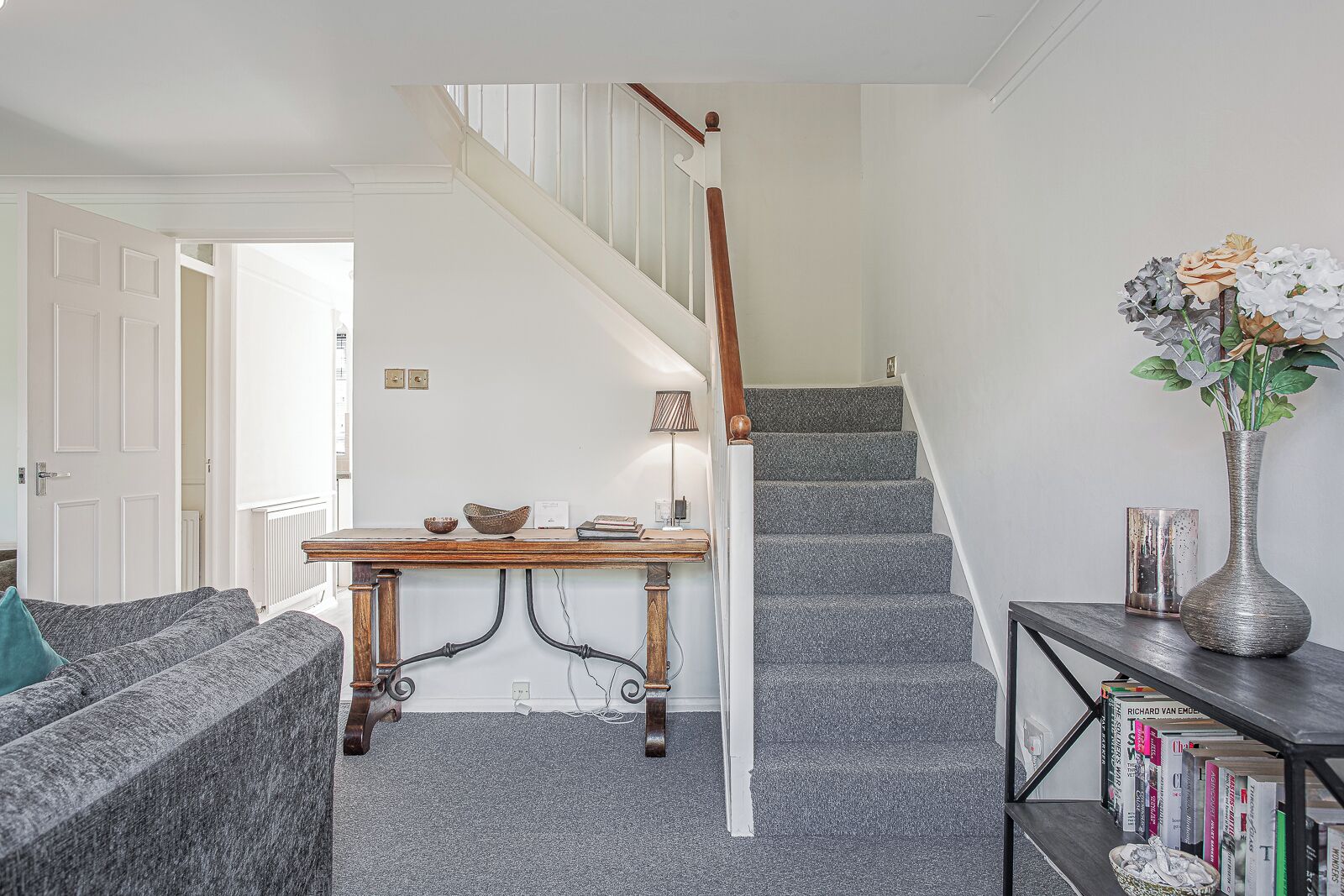 Una escalera con barandilla de madera y escalones alfombrados, una mesita con objetos decorativos y una estantería con libros.
