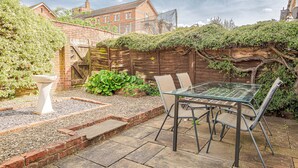 A patio with a glass table and chairs, surrounded by a brick wall and greenery. - Central 2BD with Garden and Free Parking (Cheltenham)