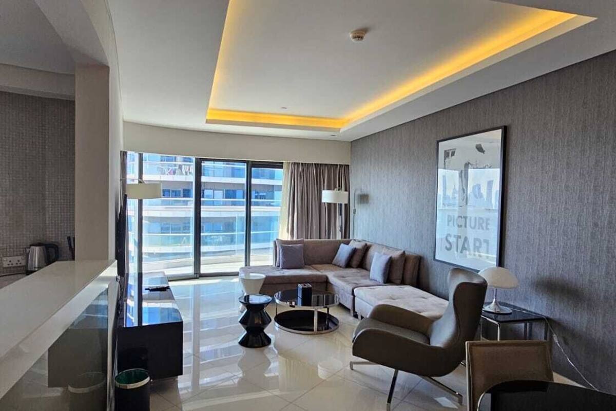 A modern living room with a sofa, armchairs, and a coffee table. There is a large window with a view of buildings.