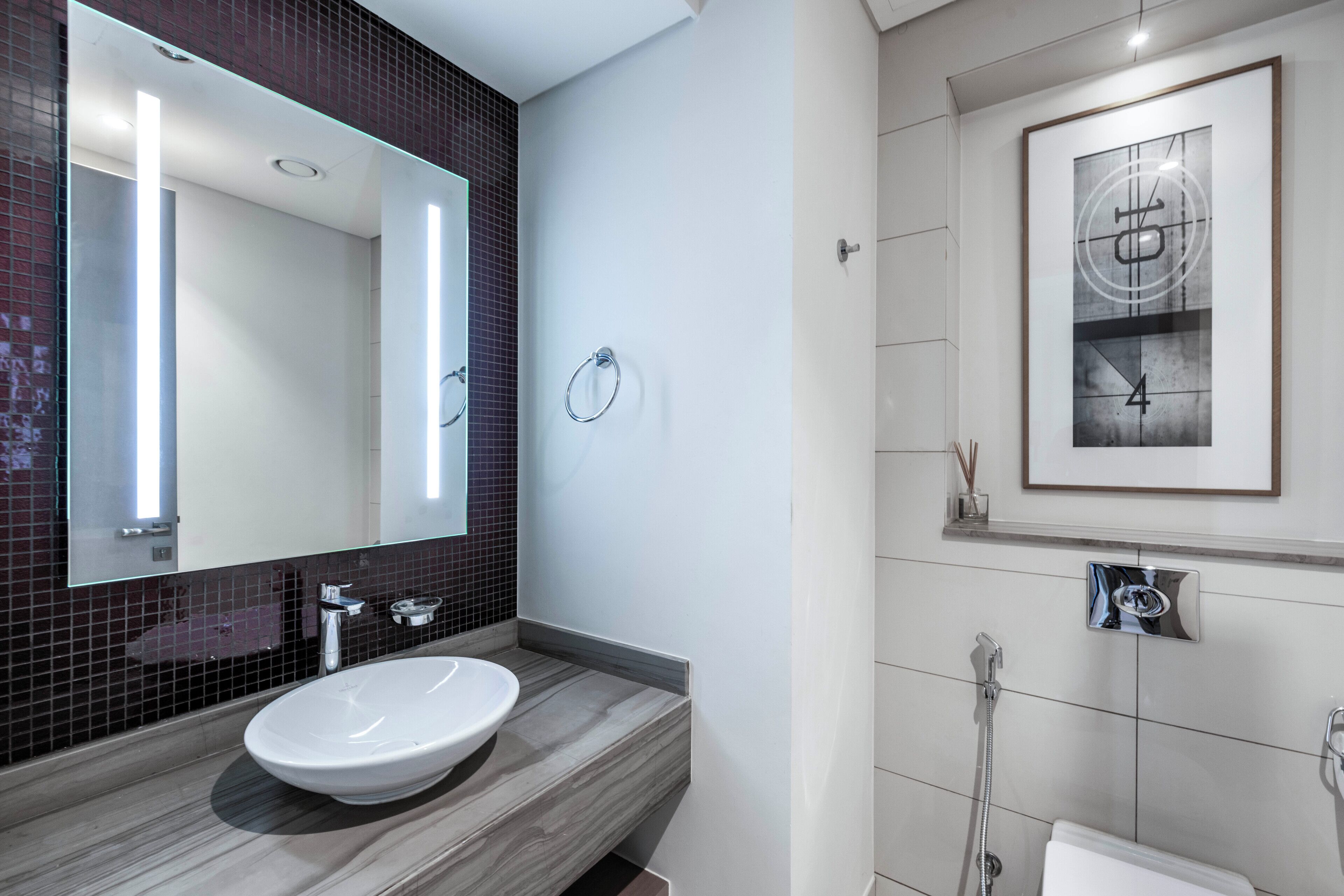 Un baño moderno con un espejo grande, un lavamanos blanco y una obra de arte enmarcada en la pared.