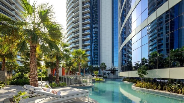 Ein modernes Hotel mit einem zentral gelegenen Schwimmbad, umgeben von Palmen und Hochhäusern.