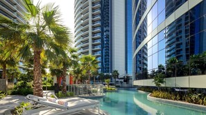 Un hotel moderno con una piscina central, rodeado de palmeras y edificios altos.