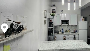 Une cuisine moderne avec des meubles blancs, un plan de travail en marbre, une horloge et des luminaires suspendus.
