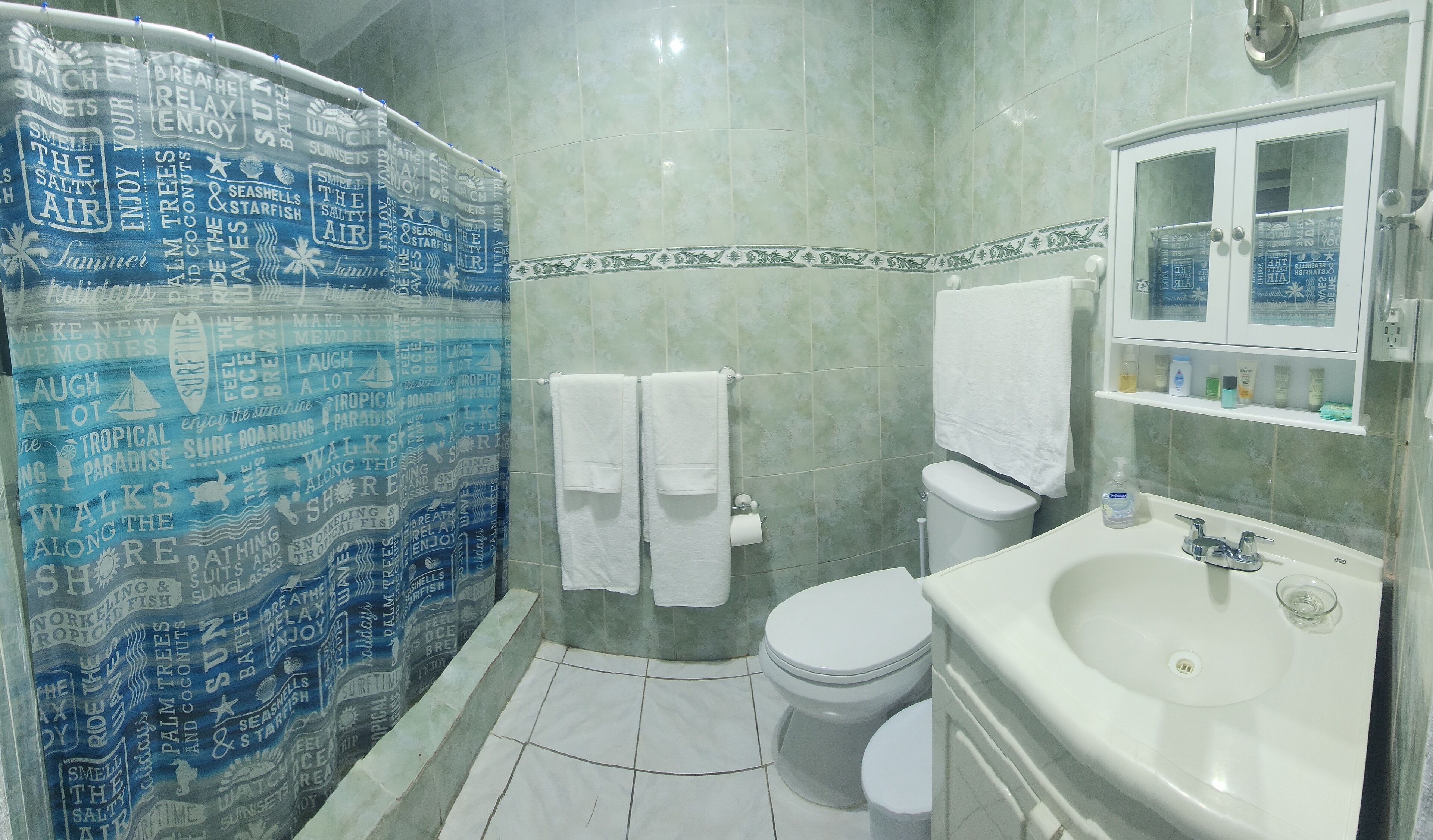 Een badkamer met een douchegordijn met nautische zinnen, een toilet, een wastafel en een spiegelkast.