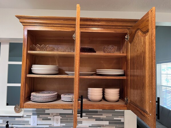 Un armario de madera con varios estantes, algunos con platos y cuencos, y un reverso con azulejos.