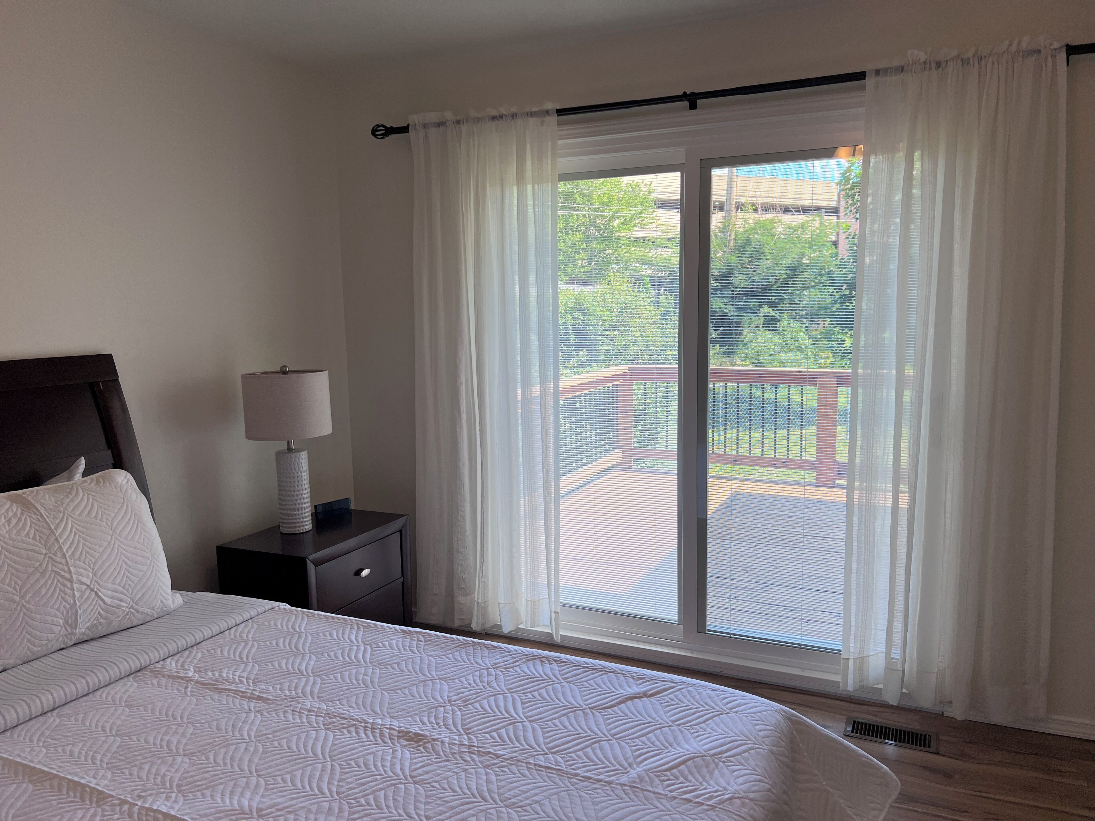 Una camera da letto con un letto, un comodino con una lampada e vista su un balcone con ringhiera.