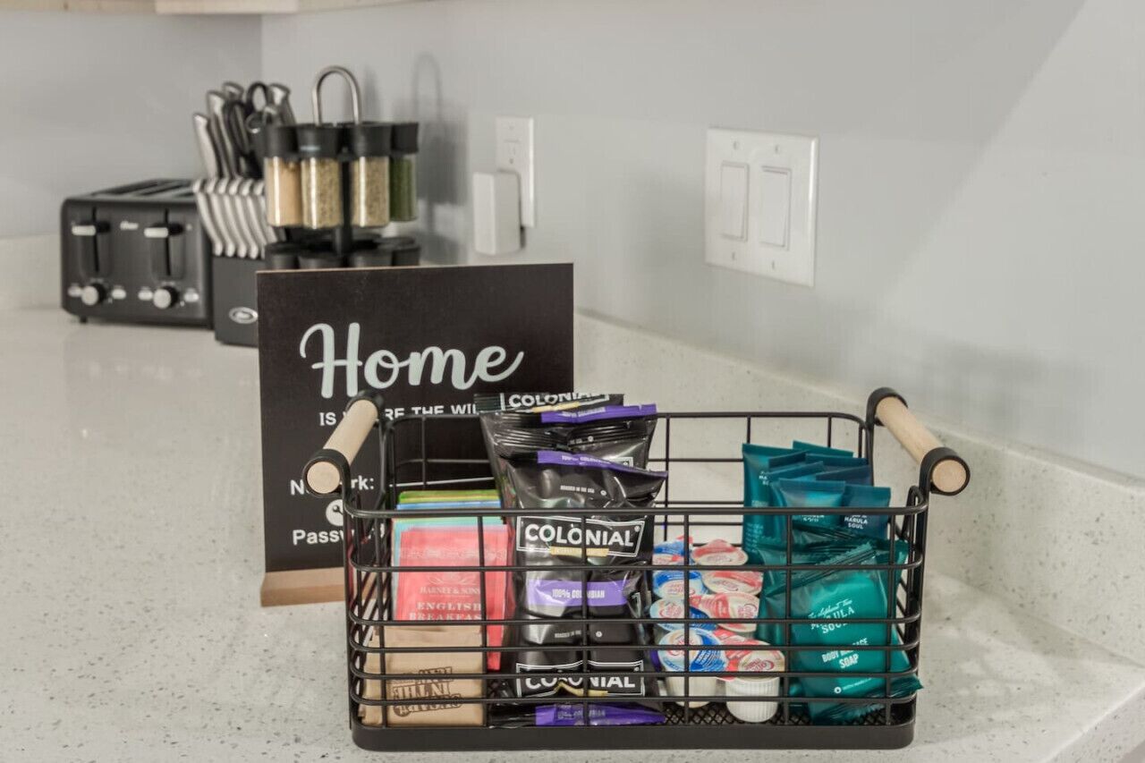 A kitchen counter with a basket of snacks, a coffee maker, and a sign that reads "Home is the Wild".