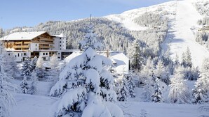 Une station de montagne enneigée, avec un immeuble à plusieurs étages doté de balcons et une piste de ski en arrière-plan.