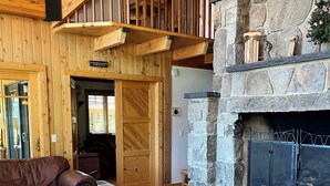 L’intérieur chaleureux d’un chalet avec une cheminée en pierre, des meubles en bois et un balcon doté d’une balustrade en bois.