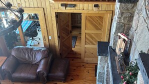 Un intérieur en bois avec une mezzanine, une cheminée en pierre et une vue sur l’extérieur.