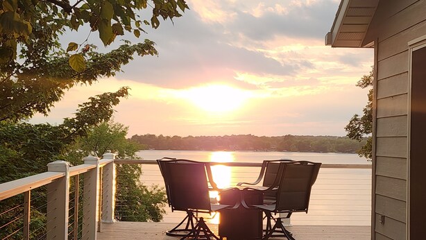 A wooden deck with two chairs and a bench, overlooking a body of water during sunset.