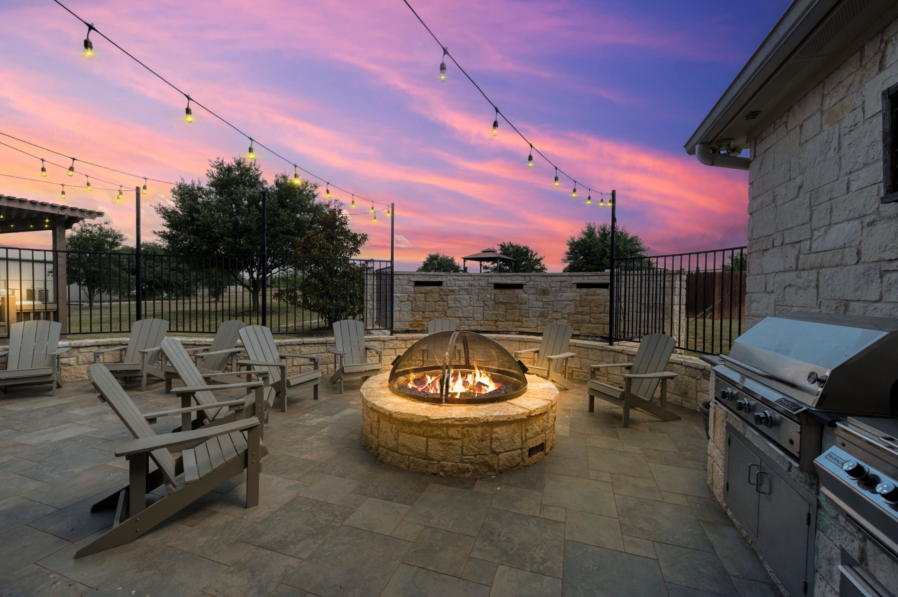 An outdoor patio with a stone fire pit, seating, and a grill area.