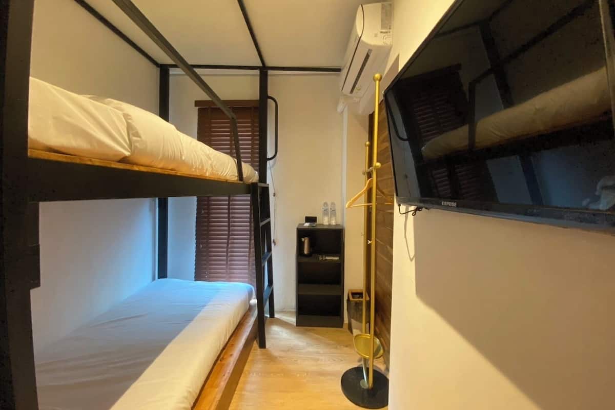 A narrow room with bunk beds, a small shelf with bottles, and an air conditioning unit.