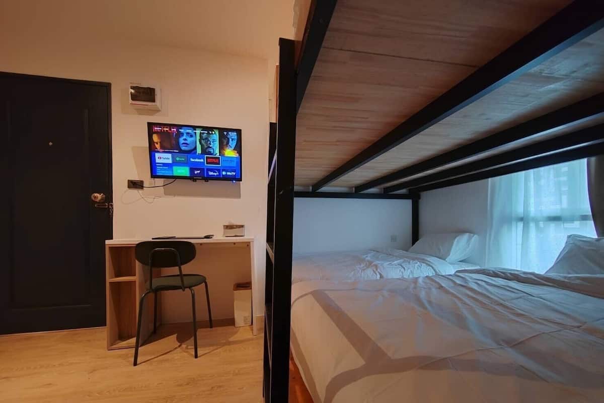 A compact room with a bunk bed, a desk with a chair, and a TV mounted on the wall displaying various streaming services.