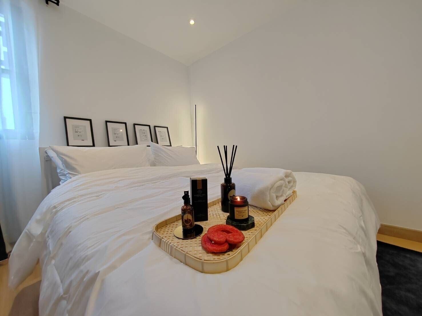 A hotel room with a neatly made bed, a tray with candles and a bottle, and framed pictures on the wall.