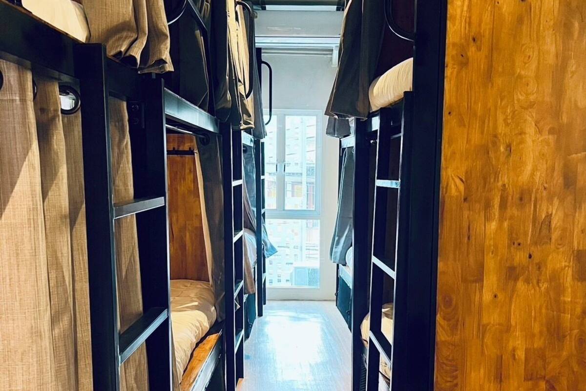A narrow hallway with bunk beds on either side, wooden walls, and a window at the end.