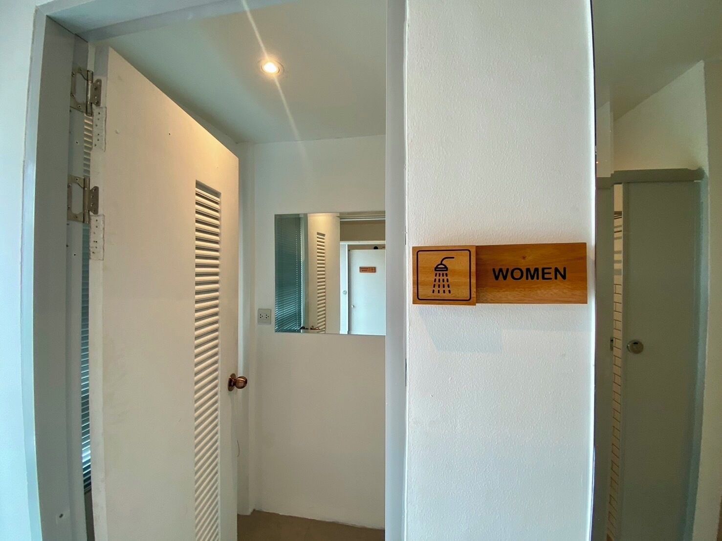 A hallway with a wooden sign indicating a women's restroom, a door with a mirror, and a ceiling light.
