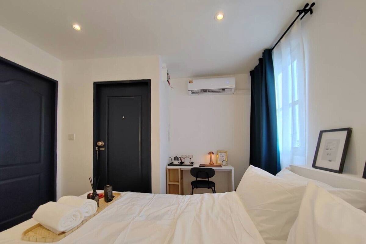 A hotel room with a bed, a desk, and a chair. There is an air conditioning unit on the wall.