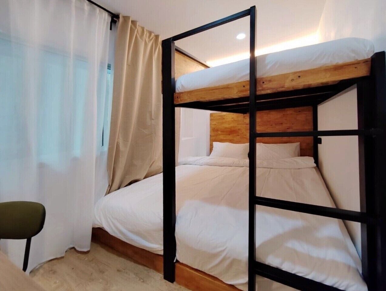 A bunk bed with a wooden headboard and white bedding in a room with a curtain and a chair.