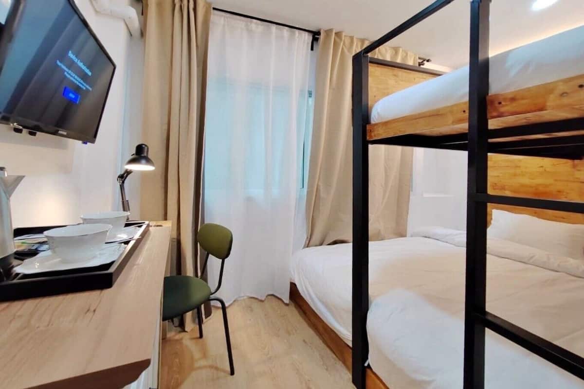 A bunk bed room with a desk, chair, and a TV on the wall.