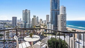 Ein Balkon mit Tisch und Stühlen mit Blick auf eine Stadtlandschaft aus hohen Gebäuden und einem Strand.
