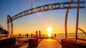 Ein Metallbogen mit der Aufschrift "SURFERS PARADISE" vor einem Sonnenuntergang.