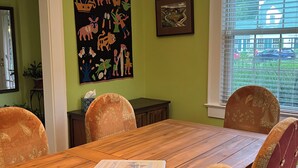 Ein Essbereich mit einem Holztisch, rot gepolsterten Stühlen, einer Hängelampe und einer Wand mit einem farbenfrohen Gemälde.