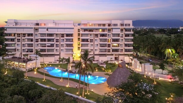 A multi-story hotel with a swimming pool, surrounded by palm trees and well-lit pathways.