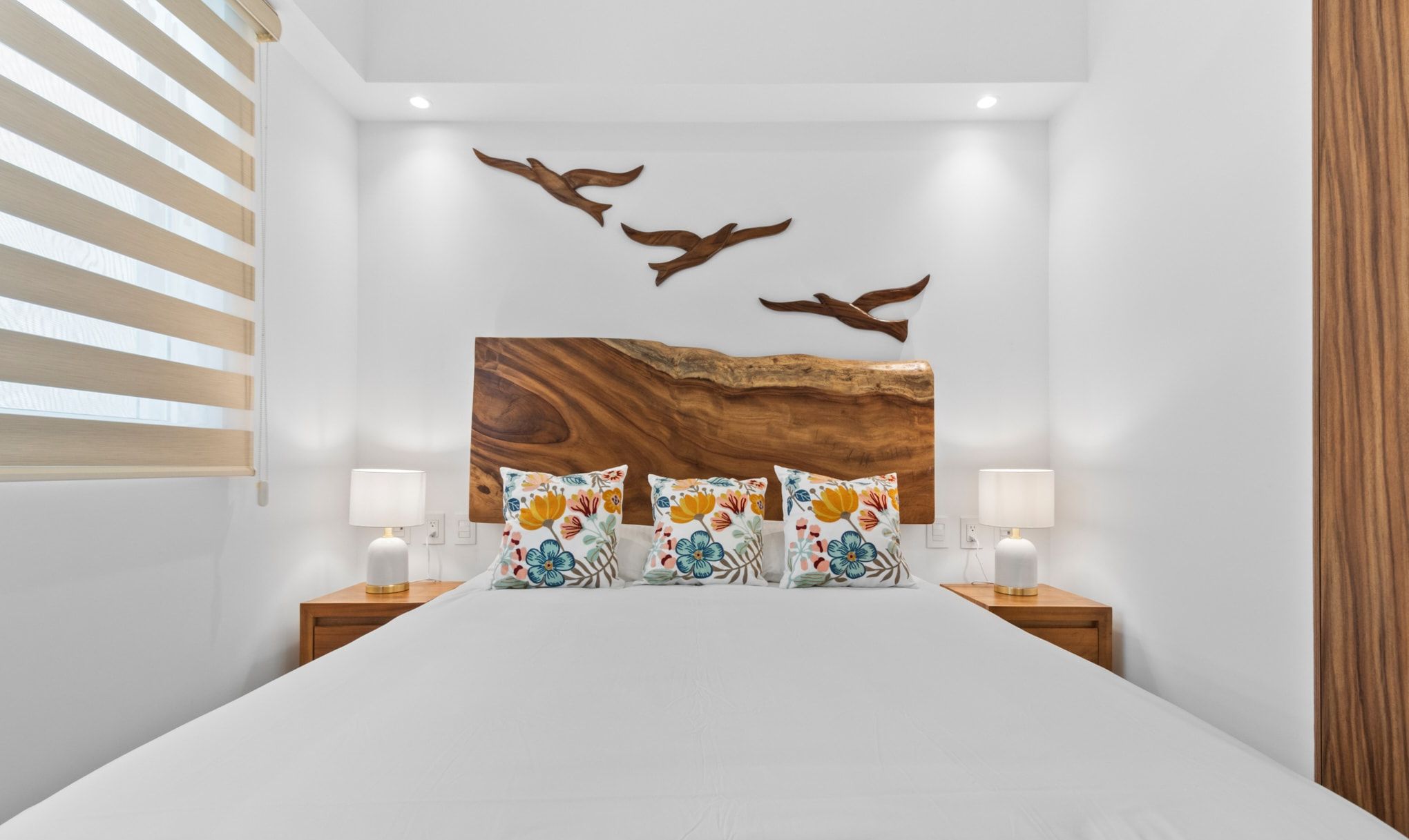Un dormitorio con una cama grande, dos lámparas de noche, un cabecero de madera y un cuadro con pájaros.