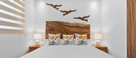 A bedroom with a large bed, two bedside lamps, a wooden headboard, and a wall art piece of birds.