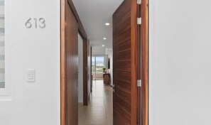 Un pasillo con una puerta de madera, una pared blanca con el número 613 y vistas a un balcón con una planta.
