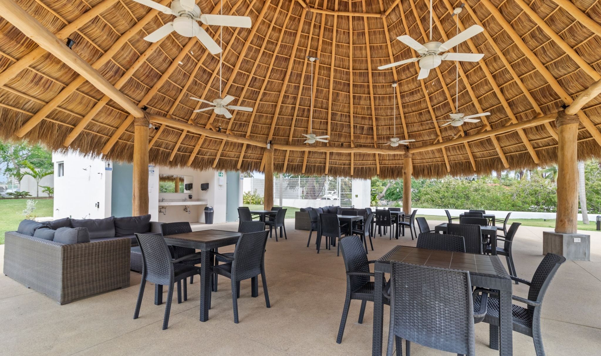 An outdoor patio with thatched roof, wicker furniture, and ceiling fans.