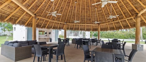 An outdoor patio with thatched roof, wicker furniture, and ceiling fans.