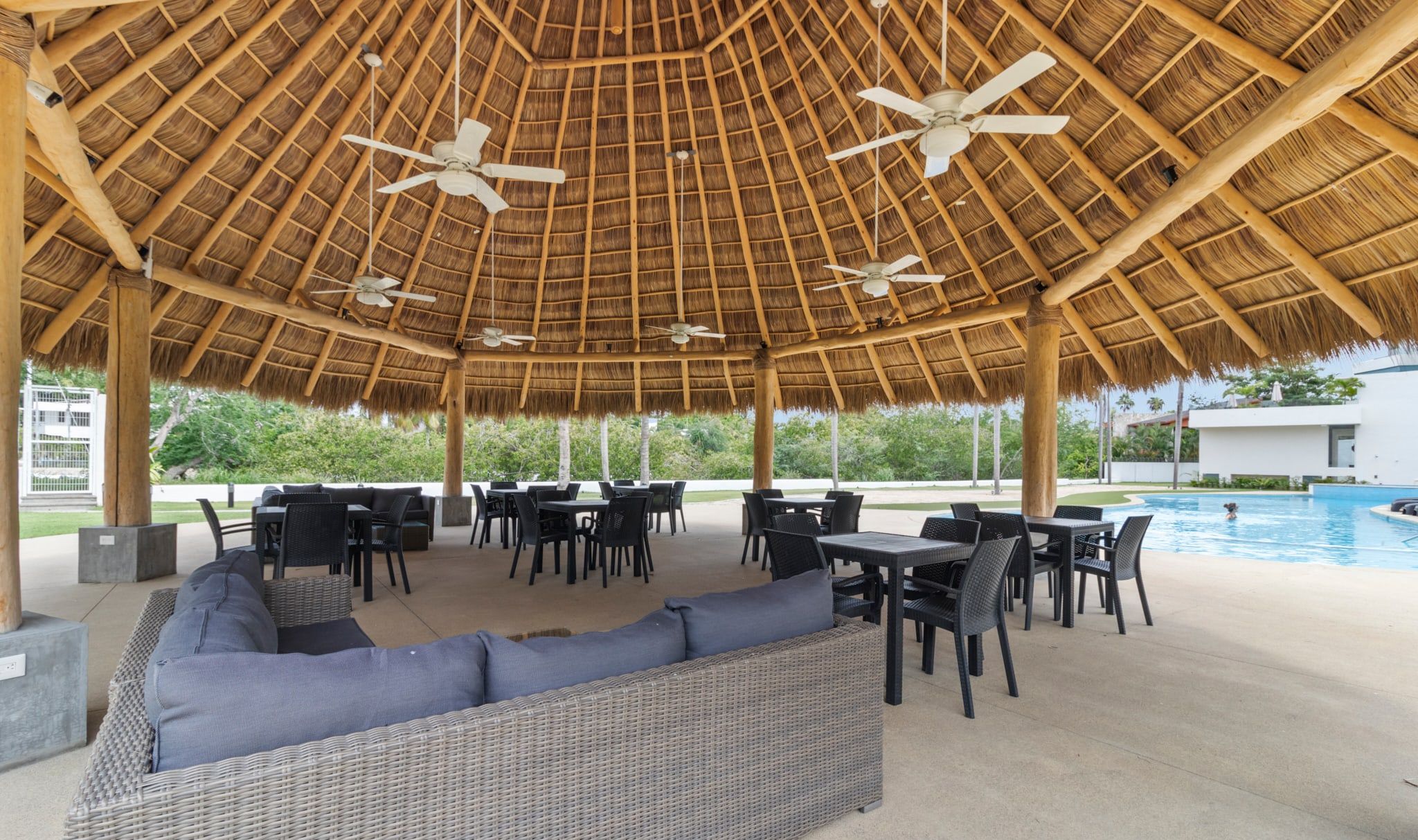 An outdoor seating area with tables and chairs, a pool, and a thatched roof structure.