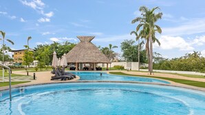 A swimming pool with lounge chairs and a thatched-roof building in the background.