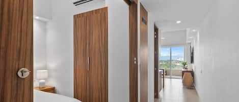 Pasillo de hotel con puertas de madera, una cama, una mesita de noche y vistas al exterior.