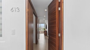 A hallway with a wooden door, a number '613' on the wall, and a view of the outside.