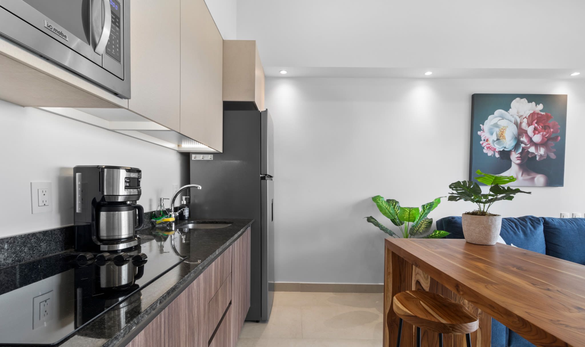 Una cocina moderna con cafetera integrada, refrigerador y un comedor con mesa de madera y sofá azul.