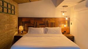 Ein ordentlich bezogenes Bett in einem Zimmer mit Backsteinwand und Holzpaneel-Kopfseitenverkleidung. Es gibt zwei Nachttische mit Lampen.