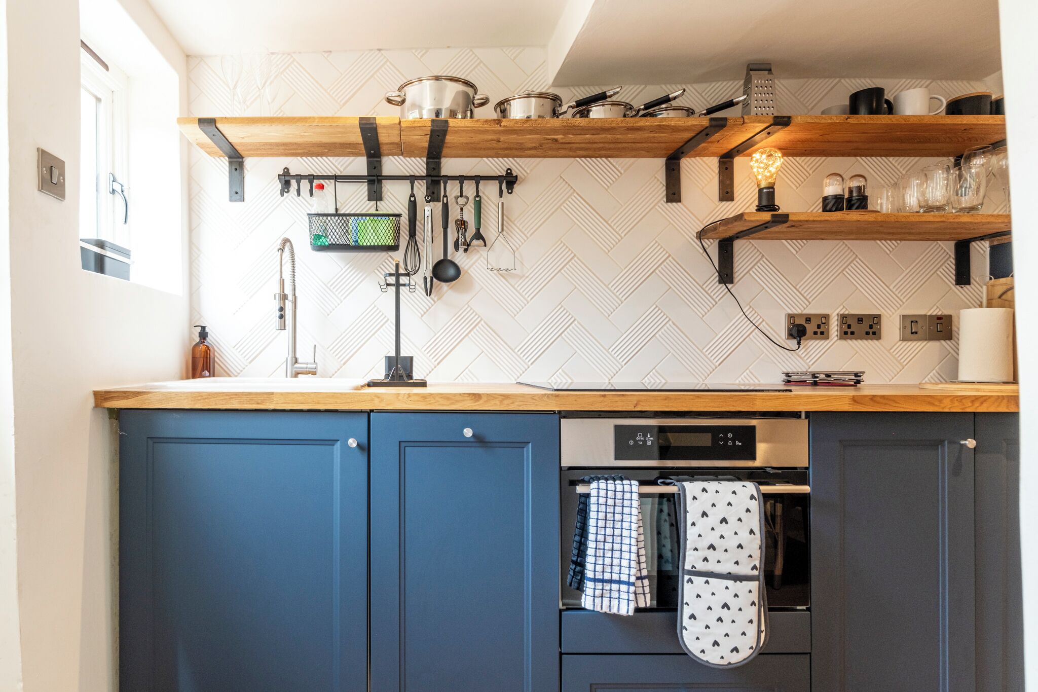 A kitchen with blue cabinets, a wooden countertop, hanging utensils, and a built-in oven.
