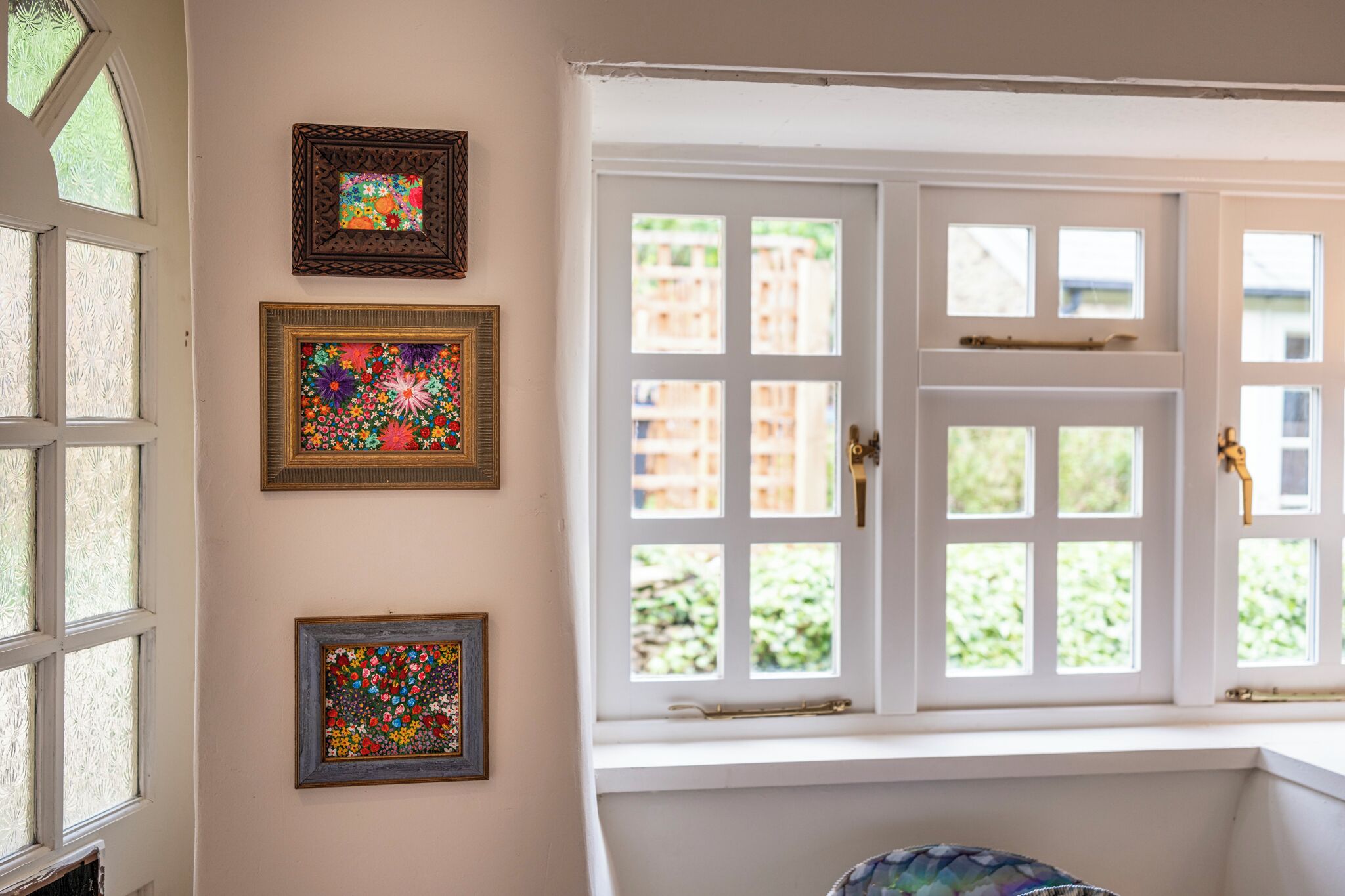 Een kamer met een groot raam, een deur en drie kunstwerken in lijsten aan de muur.