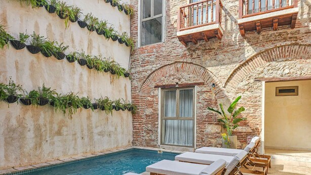 Zona piscina con sedie a sdraio, un muro in mattoni con piante pensili e un balcone in legno.