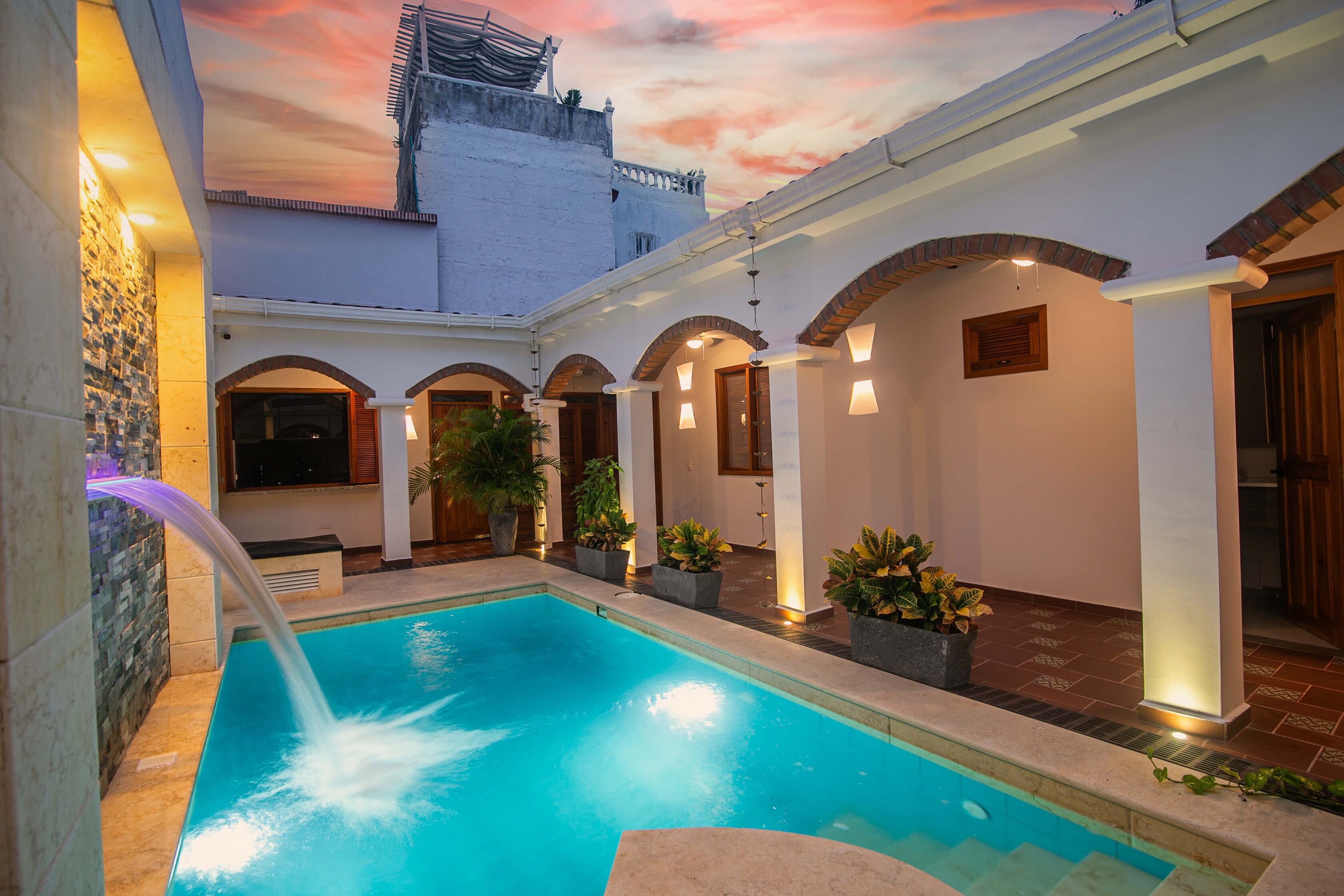A swimming pool with a water feature, surrounded by a courtyard with arches and potted plants.