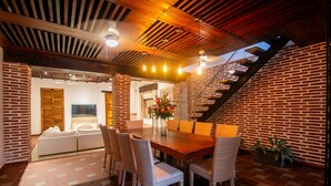 Un comedor con mesa de madera, sillas de mimbre y un muro de ladrillo.