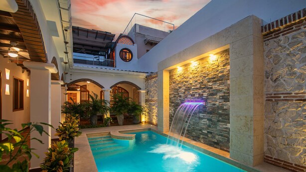 Piscina interior con caída de agua, rodeada de paredes de piedra y plantas en macetas.